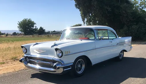 A classic white Chevrolet Bel Air parked on a road with an open field in the background on a clear sunny day.