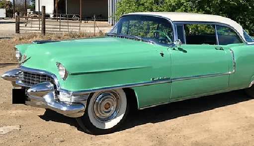 A classic mint green Cadillac car parked on a dirt road with white wall tires and chrome detailing.<br />
